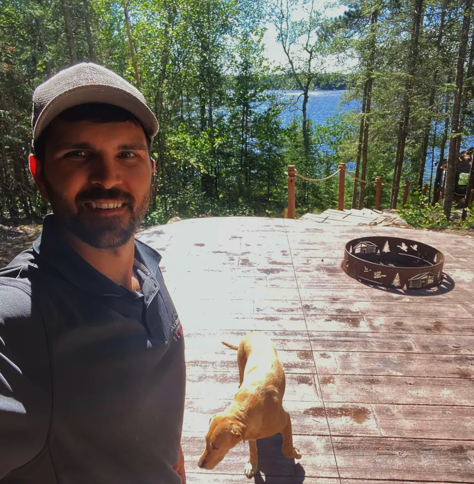 Rock Country Masonry team member standing with a dog on a hardscaped patio with a firepit by a lake.